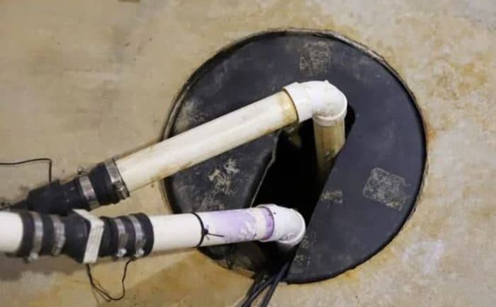 Sump pump basin with discharge piping and check valves installed in a basement floor